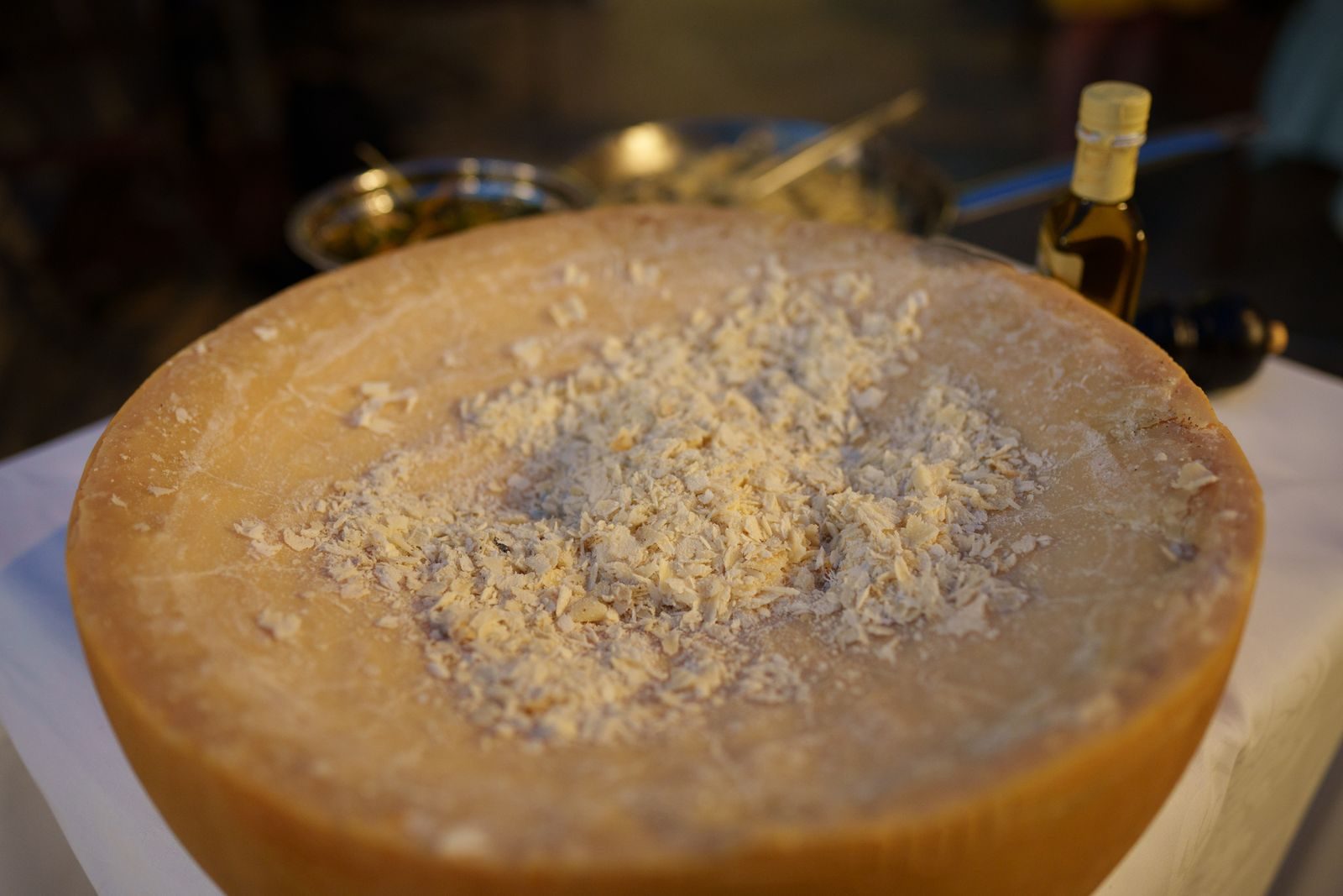 A detailed view of a Parmigiano Reggiano cheese wheel with visible cheese shavings on a table.