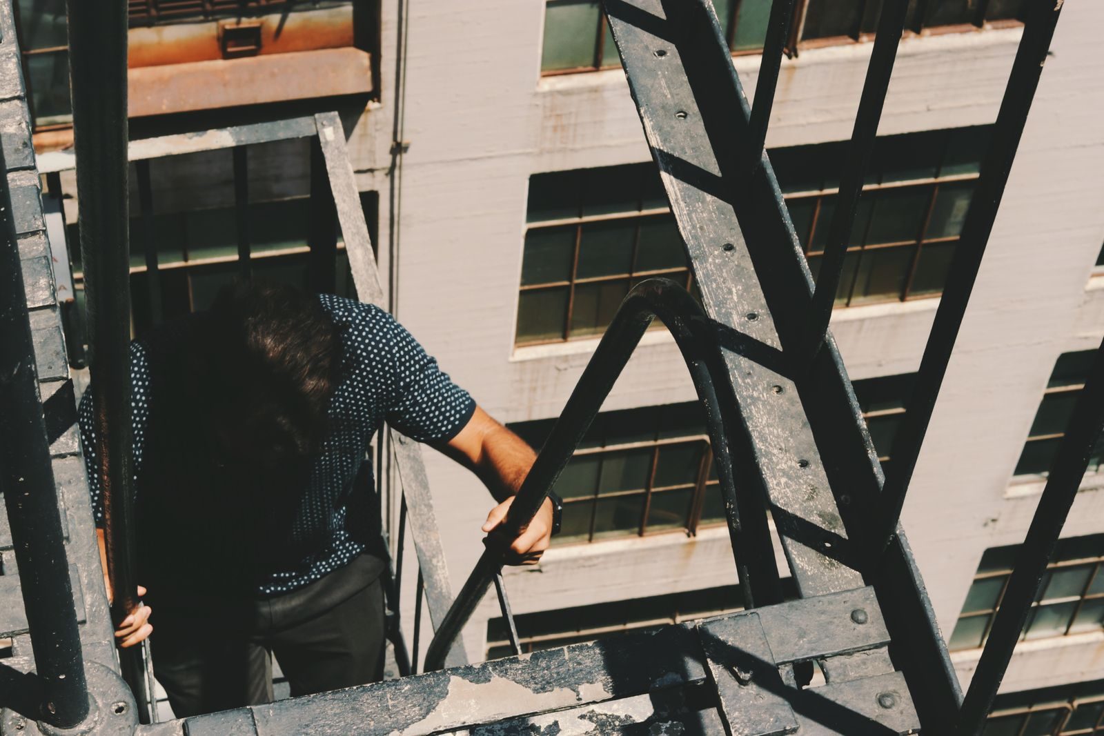 A man climbing a fire escape on a city building on a sunny day.